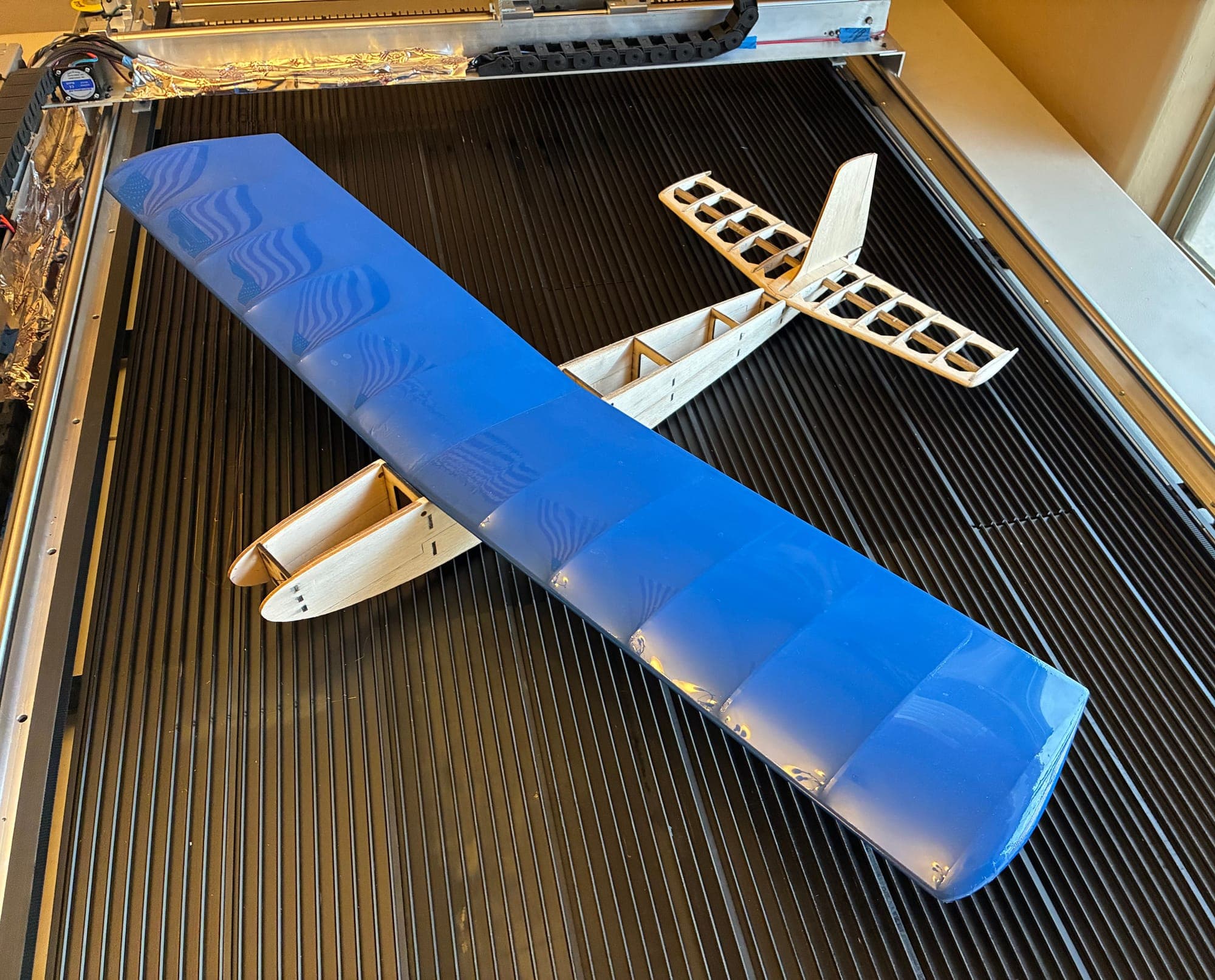 Junior Falcon build on the laser bed: blue-covered wing over the bare balsa tail structure