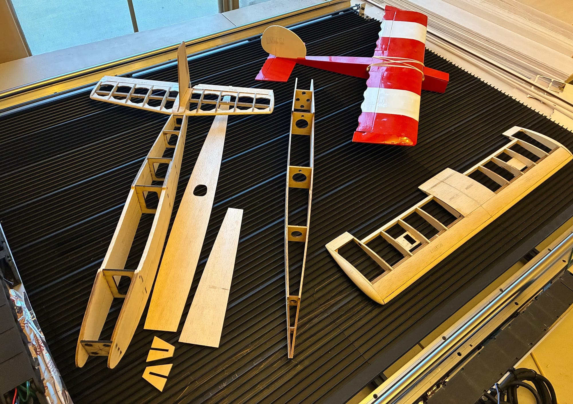 Covered red and white wing beside bare laser-cut wing and fuselage frames on the laser bed