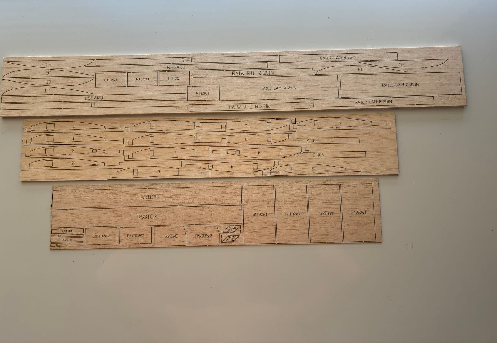 Three cut balsa sheets with engraved part labels on a light table