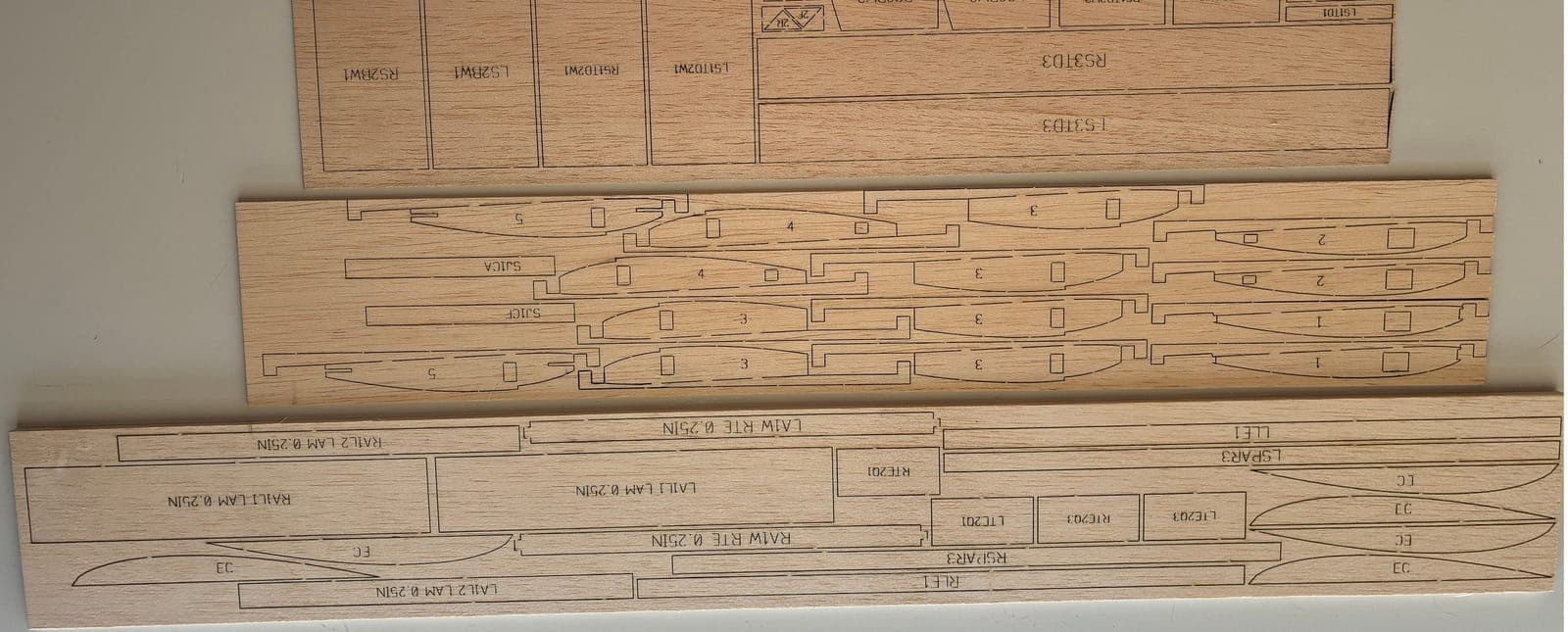 Three cut balsa sheets with engraved part labels on a light table